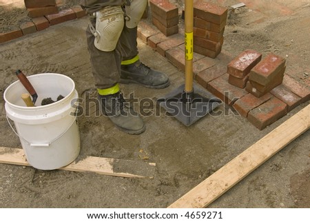 man tamping sand for brick patio