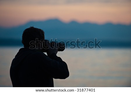 man with camera, mountains and water behind
