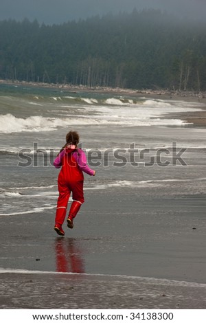 young girl  in red rain clothes skipping on Rialto Beach, Washington state coast
