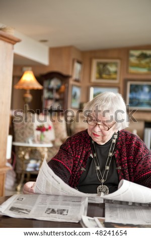 87 year old woman at home reading paper. USA