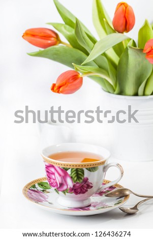 Beauty tea cup full of tea with bouquet of red tulips on white background