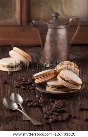 Homemade macaroons on ceramic plate with silver spoon, old silver kettle and ceramic pot on brown wooden table