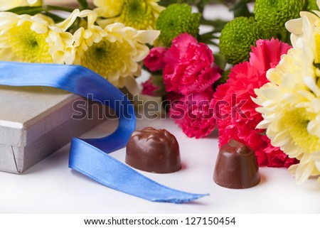 Black and white chocolate candies and bouquet of carnation and chrysanthemum flowers with blue ribbon over white