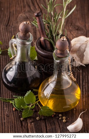 Top view on olive oil and vinegar in vintage bottles on wooden table with garlic, mint and rosemary in wooden mortar