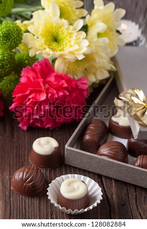 Chocolate candies, lightning candle and bouquet of carnation and chrysanthemum flowers on old wooden table