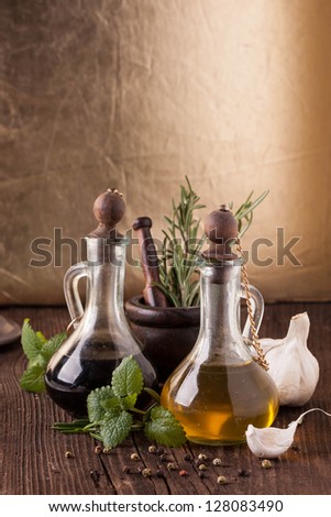 Olive oil and vinegar in vintage bottles on old wooden table with garlic, mint and rosemary in vintage mortar