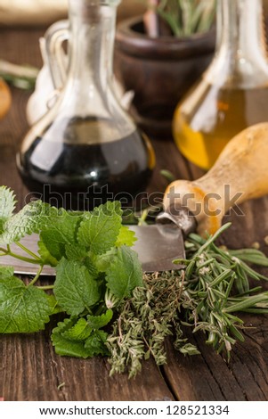 oil and vinegar in vintage bottles on wooden table, vintage knife with garlic, mint and rosemary in wooden mortar
