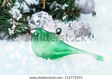 Christmas toy green glass bird on snow with christmas tree and silver balls