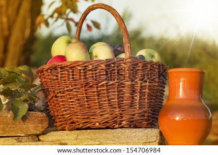 Basket of apple with ceramic pitcher on stone wall in sunshine