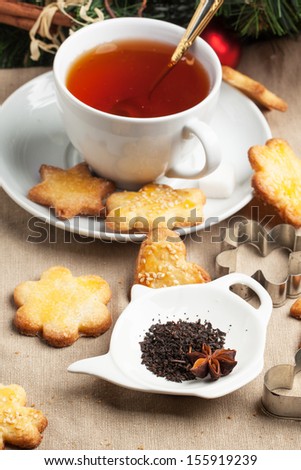 Cup of black tea served with homemade sugar cookies, dry tea leaves and metal cookie cutters over tablecloth