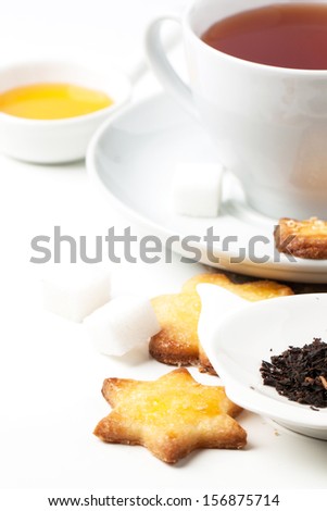 Cup of black tea served with homemade sugar cookies and dry tea leaves over white