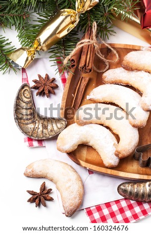 Top view on homemade sugar cookies crescent served on wooden plate with vintage cookie-cutters and gifts near christmas tree over white