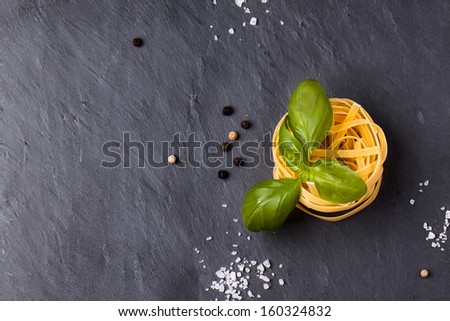 Top view on dry pasta and fresh basil served with sea salt on dark gray background