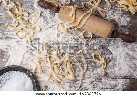 Top view on raw homemade pasta with flour, sea salt and vintage rolling pin over old wooden table