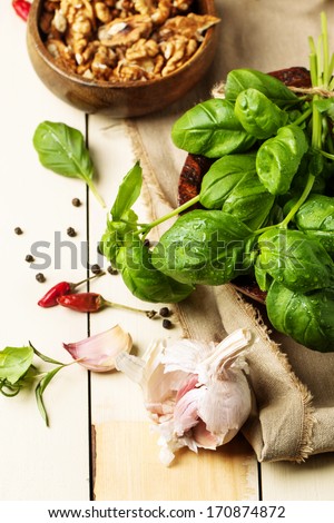 Bunch of fresh basil, bowl of walnuts, pepper and garlic served on white wooden table. See series