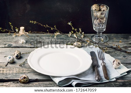 Easter table setting with vintage silverware, white plate, gray textile napkin, quail eggs and blossom branch on old wooden table