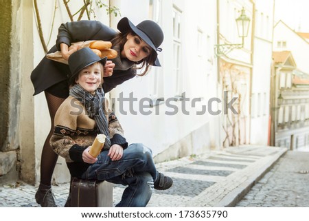 young mother and little son with vintage case in retro french style on old town street