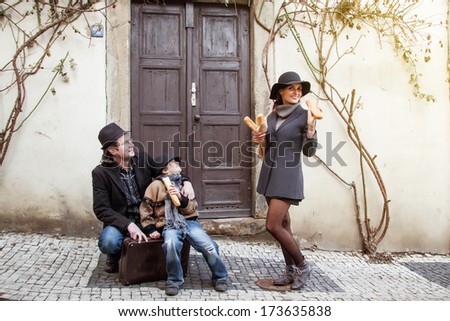 young father and little son with vintage case and young mother with bread in retro french style on old town street