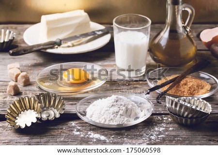 Ingredients for baking (flour, egg, brown sugar, milk) with vintage cupcake's forms on old wooden table. See series