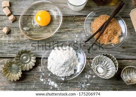 Top view on ingredients for baking (flour, egg, brown sugar, milk) with vintage cupcake\'s forms on old wooden table. See series