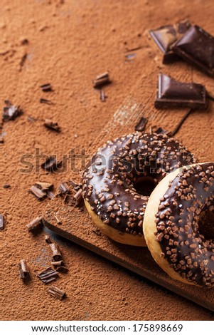 Chocolate donuts and dark chocolate served on cutting board with cocoa powder as background. See series