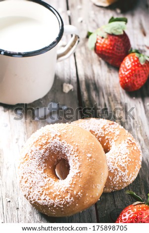 Sugar donuts and, fresh strawberries and vintage mug of milk served on wooden table. See series