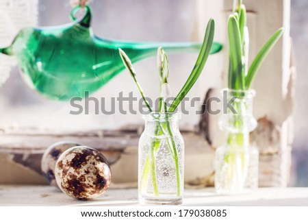 Fragment of Easter interior on old windowsill with little glass vials, blossom snowdrops, glass bird and quail eggs. See series