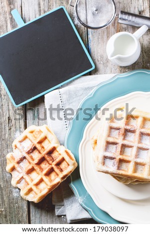 Top view on plates with fresh belgian waffles served with empty black chalkboard over old wooden table. See series