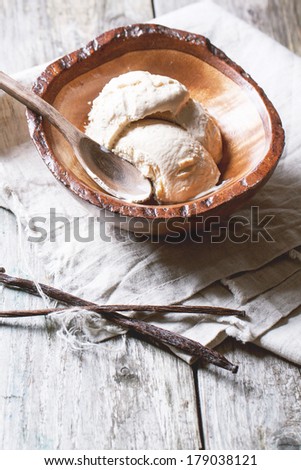 Wooden bowl with vanilla ice cream and vanilla stick on old wooden table