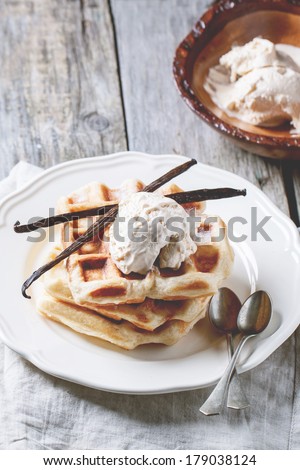 Fresh belgian waffles and bowl of ice cream, served with vanilla sticks over wooden table. See series