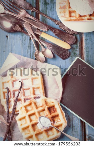 Fresh belgian waffles served with vanilla sticks and vintage cutlery over blue wooden table in instagram filter effect. See series