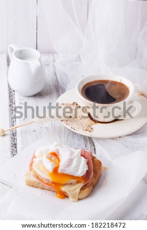 Breakfast with cup of coffee and toast with cheese and poached egg served on white wooden table. See series
