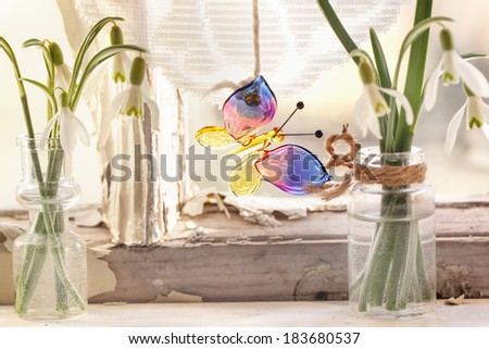 Fragment of interior on old windowsill with little glass vials, blossom snowdrops and glass butterfly. See series