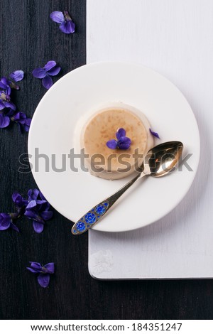 Top view on plate with caramel pannacotta served with violet flowers over black and white table