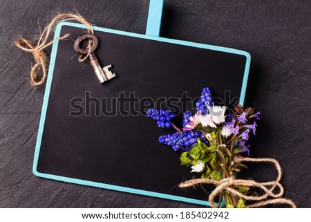 Blank chalkboard with bouquet of wildflowers ang vintage key over black