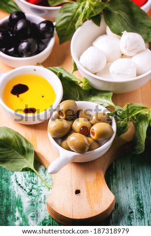 Mixed antipasti olives and mozzarella served on wooden cutting board over green wooden table.