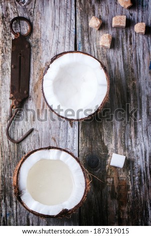 Broken coconut with coconut milk and vintage steelyard and sugar cubes on old wooden background. Top view