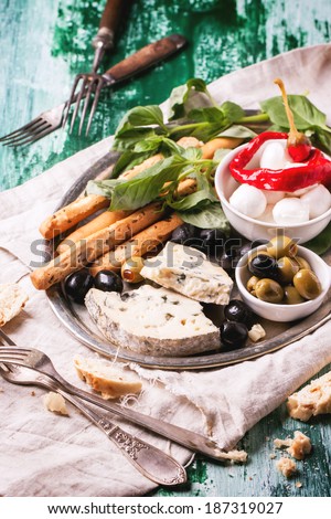 Mixed antipasti blue cheese, olives and mozzarella served on silver tray over green wooden table with vintage forks.