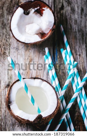 Broken coconut with coconut milk and vintage cocktail tubes on old wooden table