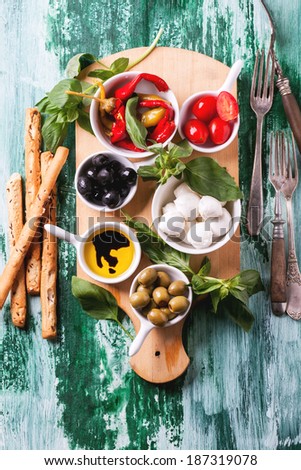 Mixed antipasti olives and mozzarella served on wooden cutting board over green wooden table with vintage fork. Top view.