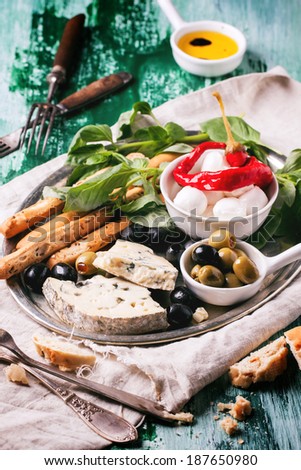 Mixed antipasti blue cheese, olives and mozzarella served on silver tray over green wooden table with vintage forks.
