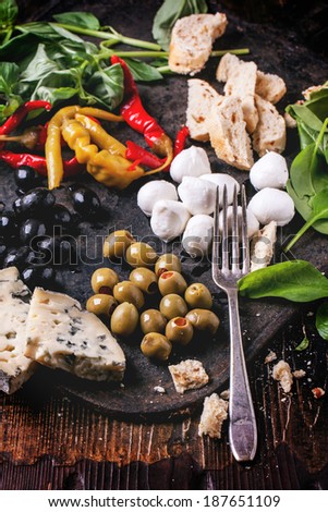 Mixed antipasti blue cheese, olives and mozzarella served on cast-iron board over wooden table with vintage fork.