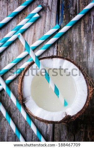 Broken coconut with coconut milk and vintage cocktail tubes on old wooden table. Top view.