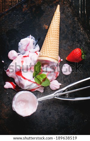 Wafer cone with strawberry ice cream with fresh strawberries, mint and metal spoon over black table. Top view.