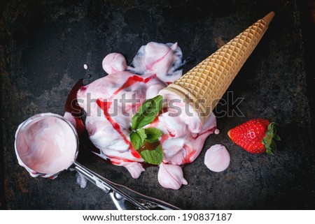 Wafer cone with strawberry ice cream with fresh strawberries, mint and metal spoon over black table. Top view.
