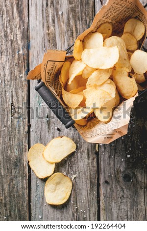 Top view on basket with potato chips with sea salt over old wooden table. See series