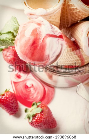 Wafer cones with strawberry ice cream with syrup and fresh strawberries served in glass jar over white textile. With Instagram filter effect.