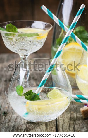 Fresh homemade lemonade with lemon, lime and mint in glasses with vintage cocktail tube over wooden table.