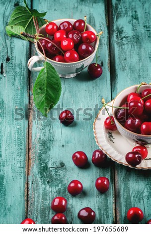 Fresh cherries in vintage tea cups on blue wooden table