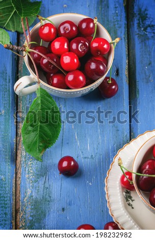Fresh cherries in vintage tea cups on blue wooden table